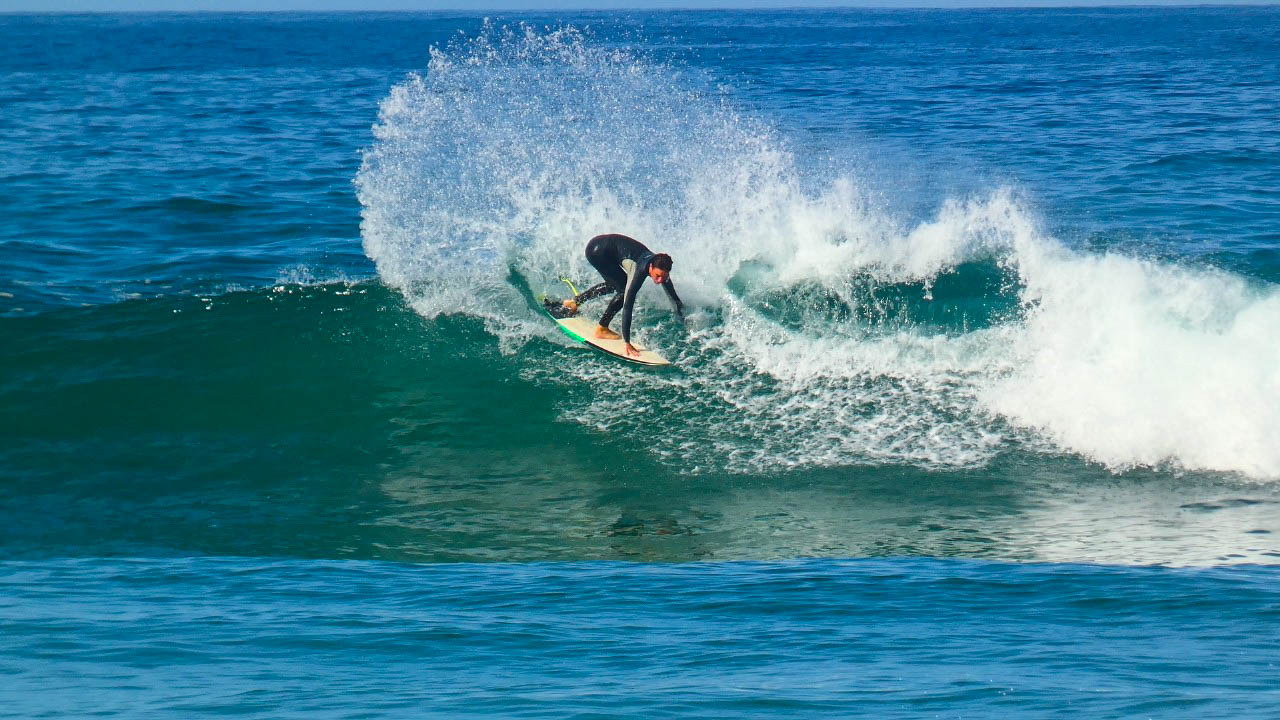 Surfer riding the long right-hand wave at Imsouane Bay with the headland in the background
